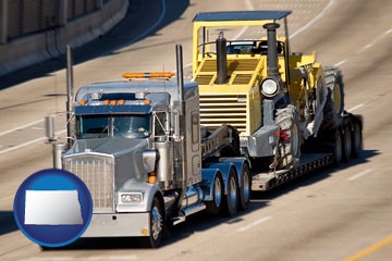 a semi-truck hauling heavy construction equipment - with North Dakota icon